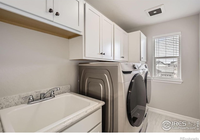 laundry room featuring separate washer and dryer, a sink, cabinet space, and baseboards