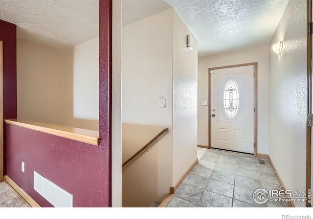 foyer entrance with visible vents, a textured ceiling, and baseboards