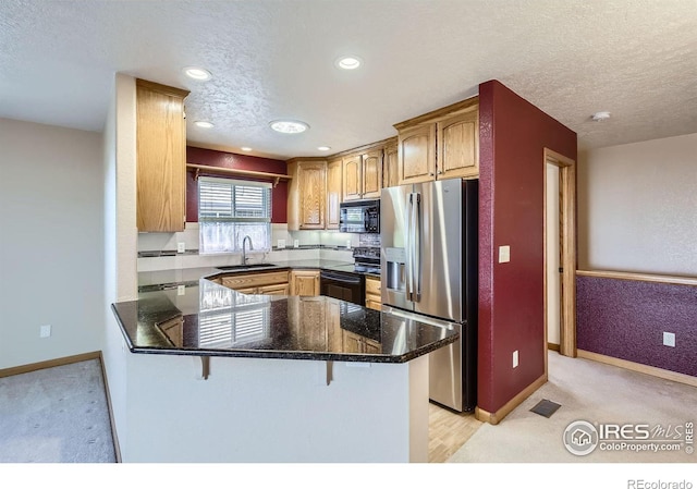 kitchen featuring a breakfast bar area, a sink, a textured ceiling, a peninsula, and black appliances