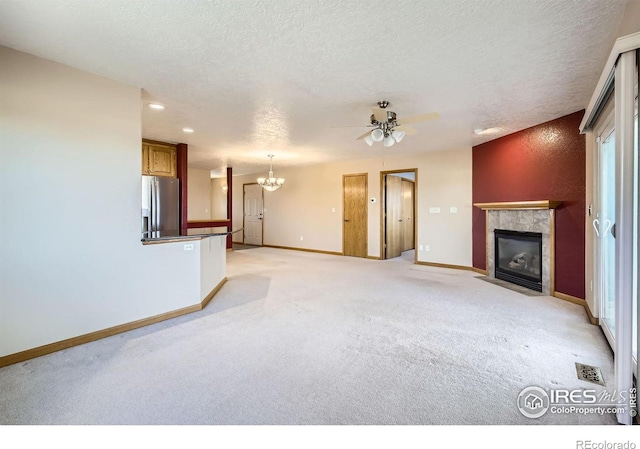 unfurnished living room with a textured ceiling, light colored carpet, ceiling fan with notable chandelier, baseboards, and a tiled fireplace