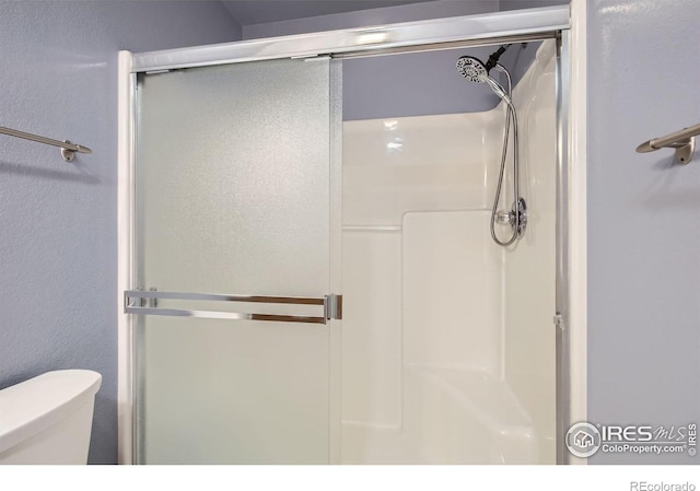 bathroom with toilet, a stall shower, and a textured wall