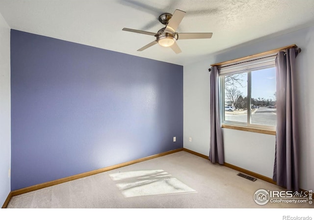 carpeted empty room featuring a textured ceiling, ceiling fan, visible vents, and baseboards