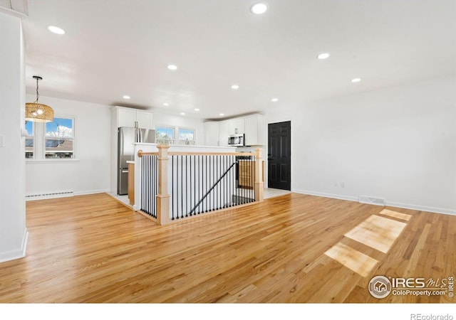 kitchen featuring appliances with stainless steel finishes, a baseboard radiator, light wood-style flooring, and white cabinetry