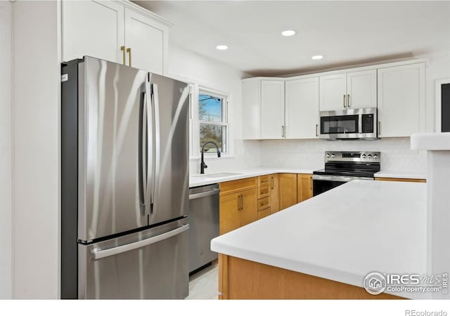 kitchen featuring tasteful backsplash, white cabinets, appliances with stainless steel finishes, light countertops, and a sink