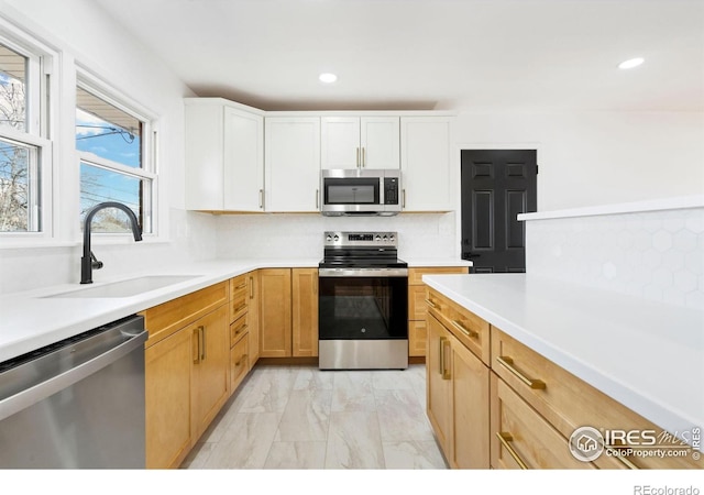 kitchen with tasteful backsplash, stainless steel appliances, light countertops, a sink, and recessed lighting