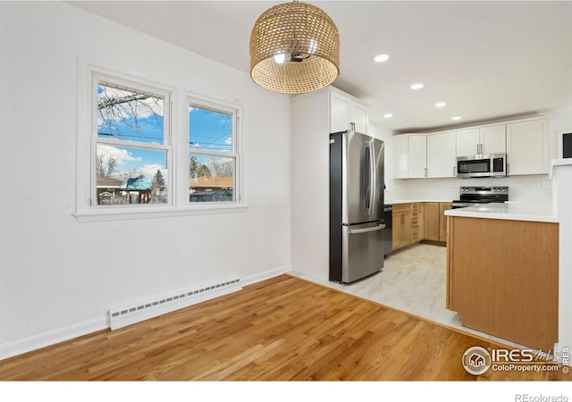 kitchen with light wood finished floors, light countertops, appliances with stainless steel finishes, a baseboard heating unit, and white cabinetry