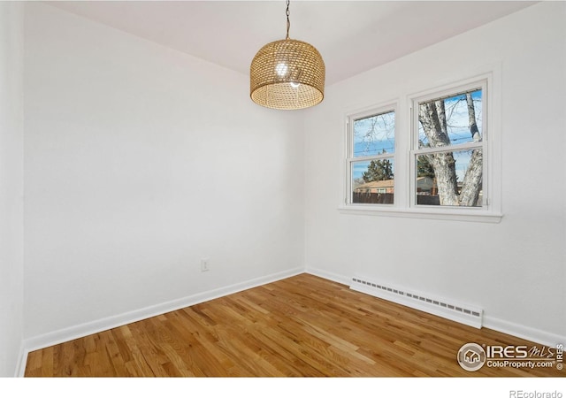 empty room with baseboards, a baseboard heating unit, and wood finished floors