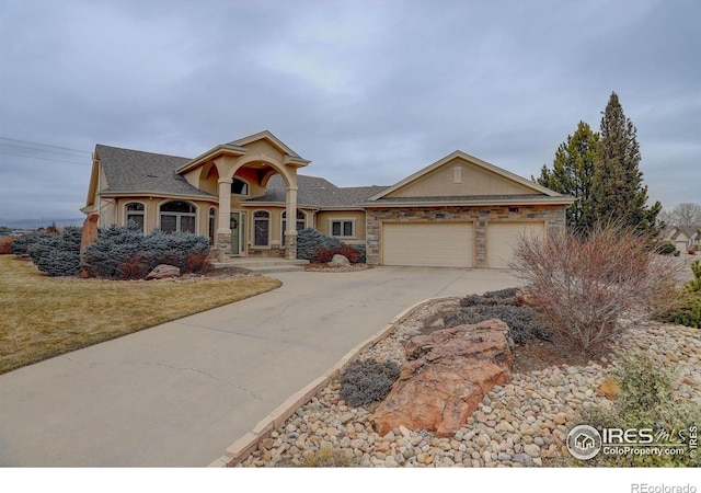 view of front of property featuring a garage, concrete driveway, stone siding, and stucco siding