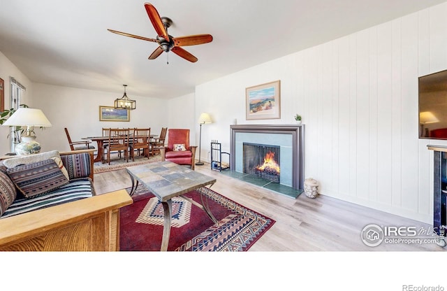 living room featuring a fireplace with flush hearth, light wood-type flooring, and a ceiling fan