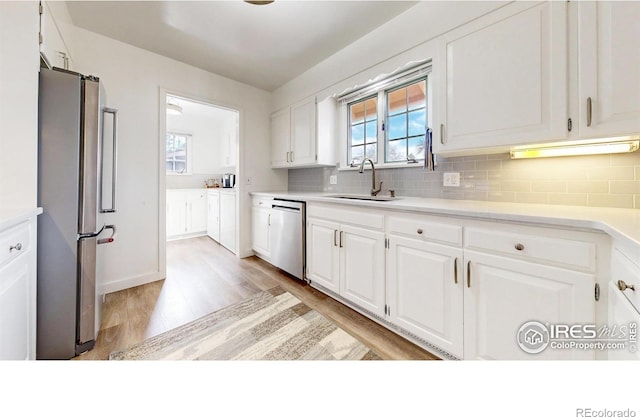 kitchen featuring appliances with stainless steel finishes, backsplash, a sink, and white cabinetry