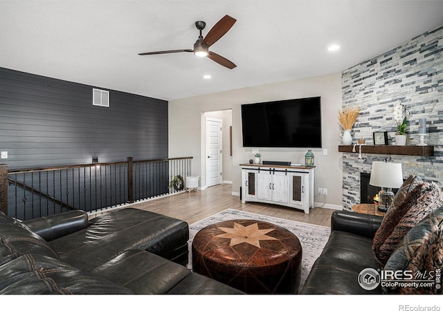 living room with a stone fireplace, wood finished floors, visible vents, baseboards, and a ceiling fan