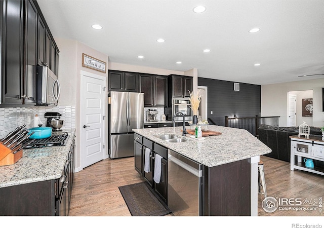 kitchen featuring open floor plan, stainless steel appliances, a sink, and light wood-style flooring