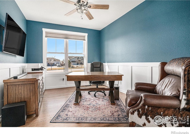 office space featuring ceiling fan, light wood finished floors, and a wainscoted wall