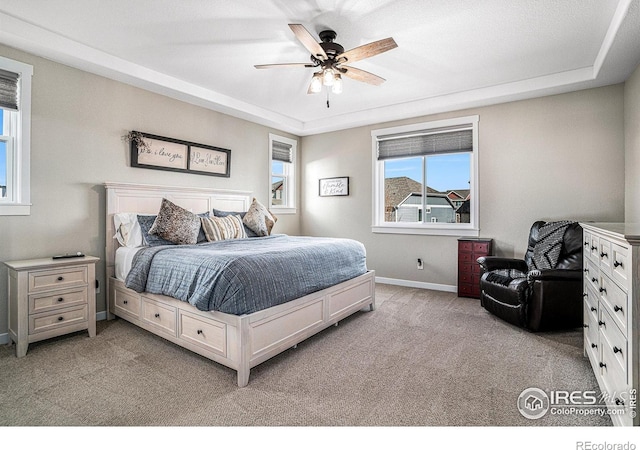 bedroom with a ceiling fan, a tray ceiling, light colored carpet, and baseboards