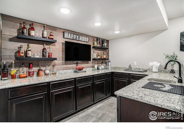 bar featuring a textured ceiling, wood walls, indoor wet bar, and a sink