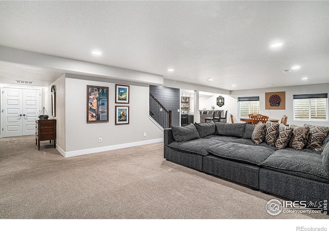 carpeted living area with baseboards, visible vents, stairway, and a textured ceiling