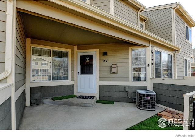 view of exterior entry with a porch, fence, and central air condition unit