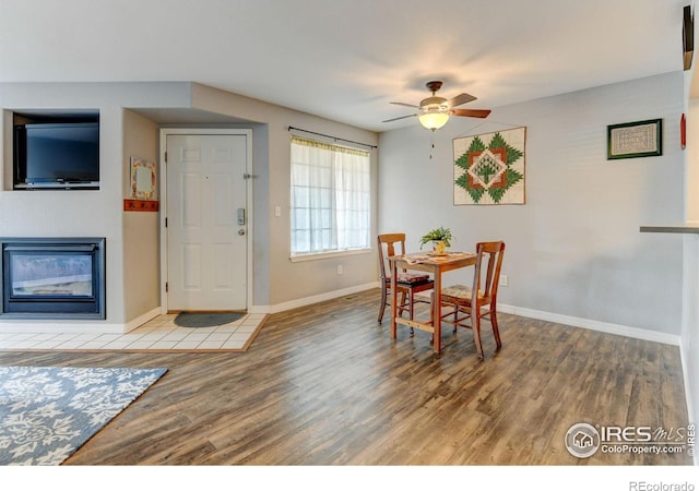 dining room featuring a glass covered fireplace, baseboards, a ceiling fan, and wood finished floors