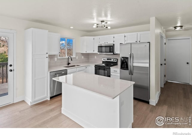 kitchen featuring light wood finished floors, white cabinets, decorative backsplash, stainless steel appliances, and a sink