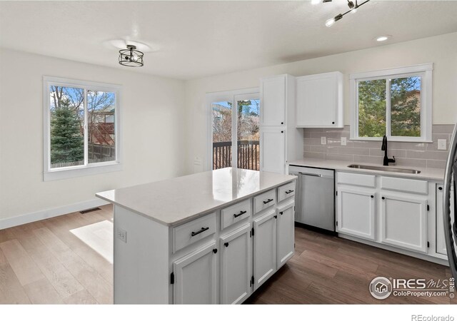 kitchen with decorative backsplash, wood finished floors, a healthy amount of sunlight, stainless steel dishwasher, and a sink