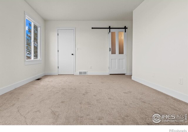 carpeted empty room with visible vents, baseboards, and a barn door