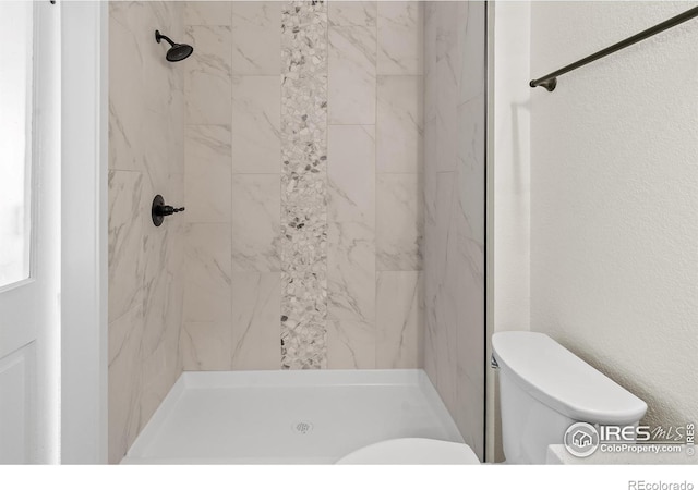 bathroom featuring a textured wall, a shower stall, and toilet