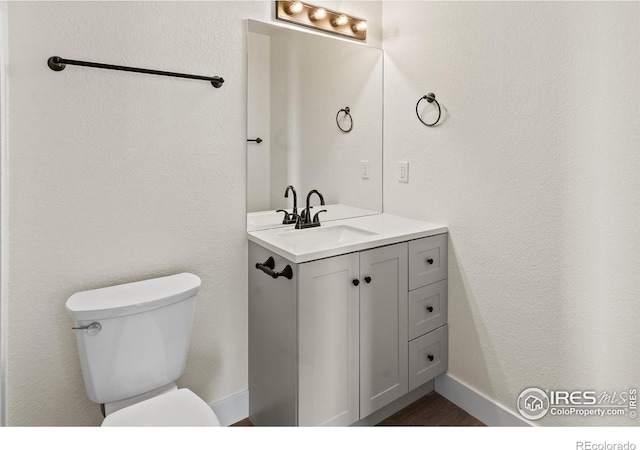 half bath featuring baseboards, a textured wall, vanity, and toilet