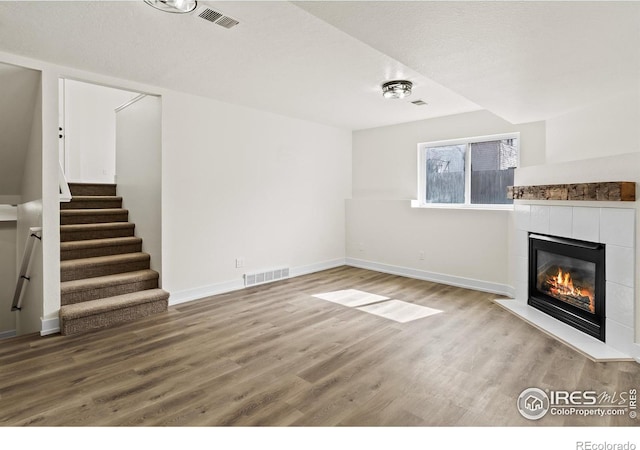 unfurnished living room with stairs, visible vents, a tiled fireplace, and wood finished floors