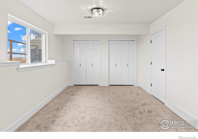 unfurnished bedroom with carpet floors, baseboards, visible vents, and two closets