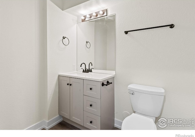 half bath with baseboards, vanity, and toilet