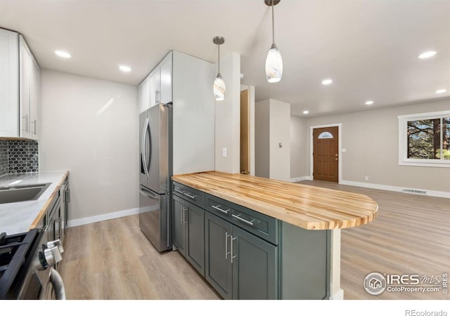 kitchen featuring light wood-type flooring, stainless steel appliances, white cabinets, butcher block counters, and decorative backsplash