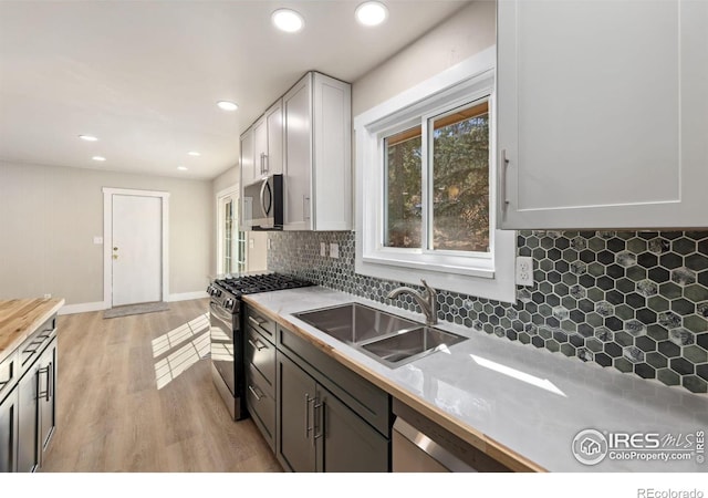 kitchen with a sink, decorative backsplash, white cabinets, light wood-style floors, and appliances with stainless steel finishes