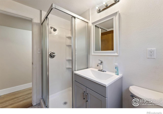 full bath featuring baseboards, toilet, a stall shower, wood finished floors, and vanity