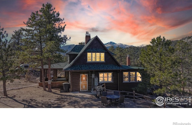 back of property at dusk featuring a shingled roof, a chimney, and faux log siding