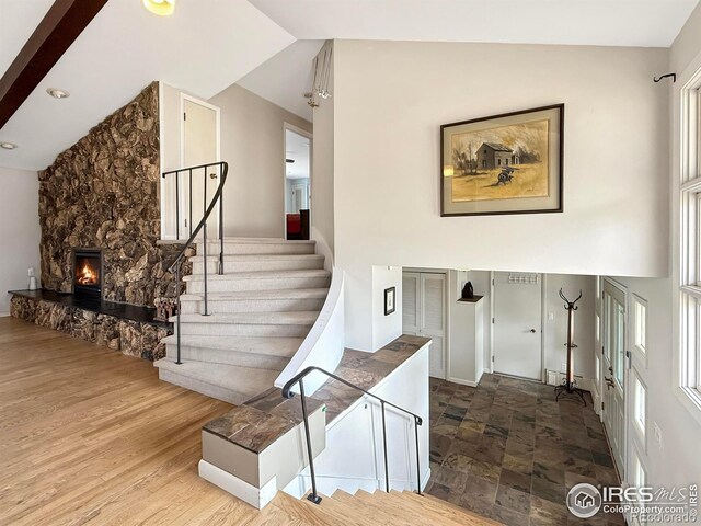 stairway featuring high vaulted ceiling, a fireplace, and wood finished floors