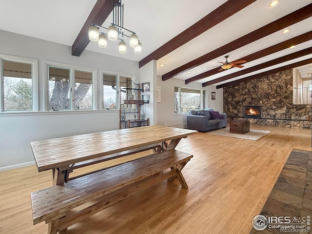 dining room featuring a fireplace, wood finished floors, beam ceiling, and a ceiling fan