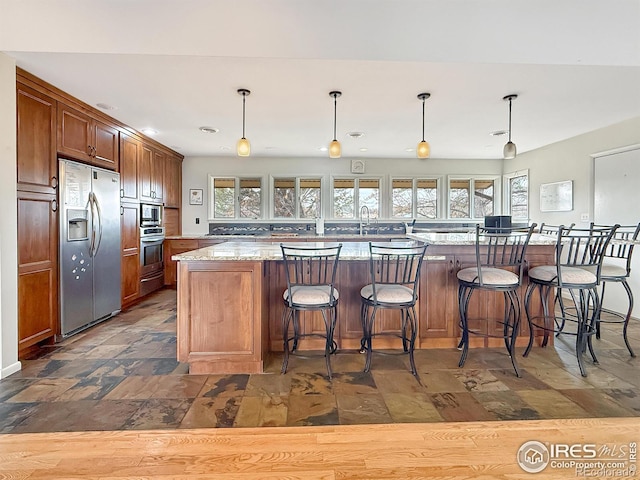 kitchen featuring stainless steel appliances, light stone counters, stone finish floor, and hanging light fixtures