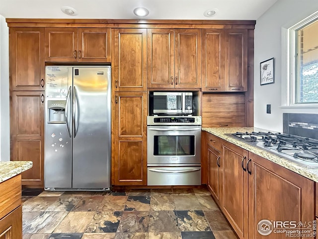 kitchen with stainless steel appliances, stone finish flooring, brown cabinets, and a warming drawer