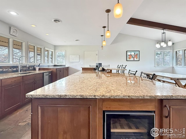 kitchen featuring a spacious island, visible vents, lofted ceiling with beams, a sink, and light stone countertops