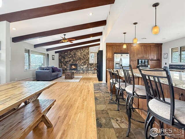 dining space featuring a wealth of natural light, beamed ceiling, a stone fireplace, and stone tile floors