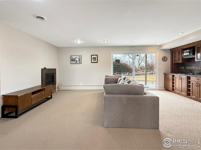 living area featuring a fireplace, a baseboard radiator, visible vents, light carpet, and wet bar