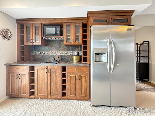 kitchen featuring stainless steel fridge, decorative backsplash, brown cabinets, open shelves, and a sink