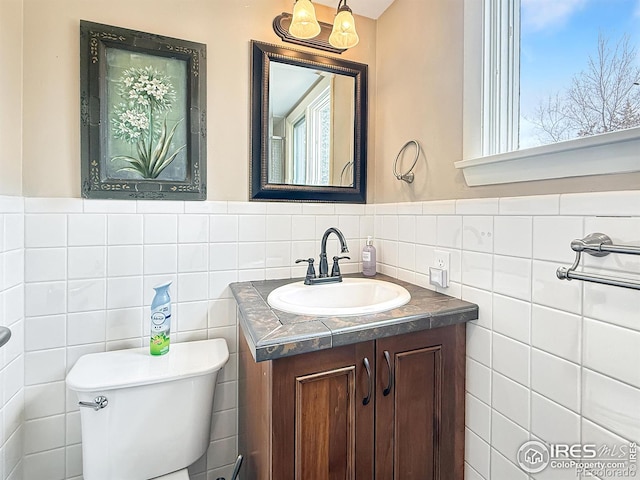 half bathroom with toilet, a wainscoted wall, vanity, and tile walls