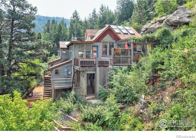 back of house featuring a view of trees, a wooden deck, and stairs