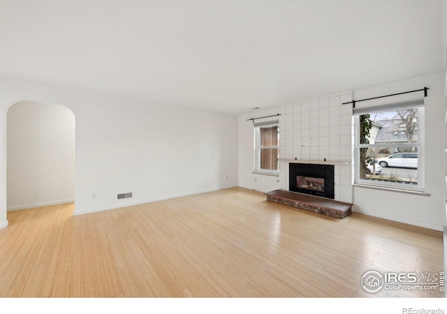 unfurnished living room with a wealth of natural light, a fireplace, wood finished floors, and visible vents