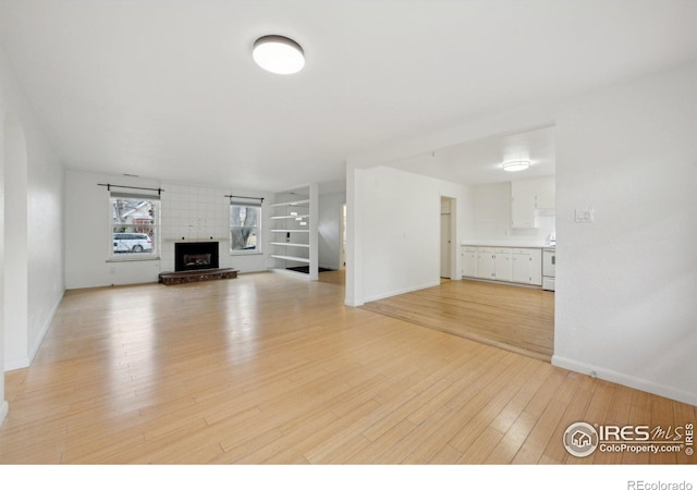 unfurnished living room featuring baseboards, a brick fireplace, and light wood-style floors