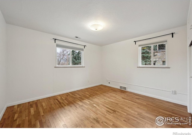 unfurnished room with visible vents, a textured ceiling, baseboards, and wood finished floors