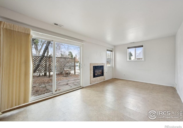 unfurnished living room with a glass covered fireplace, visible vents, baseboards, and tile patterned floors