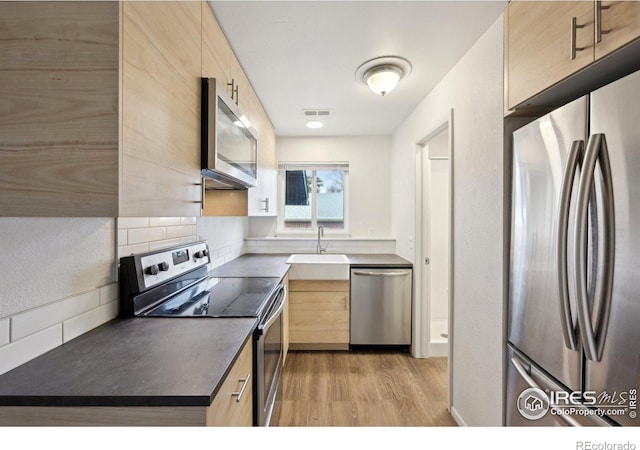 kitchen with stainless steel appliances, light brown cabinetry, dark countertops, and a sink