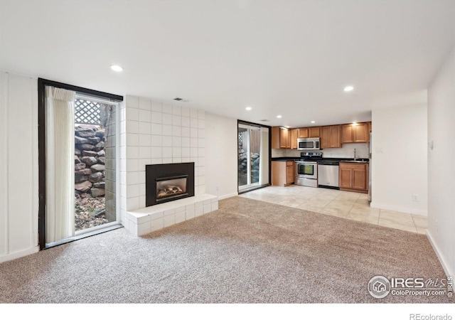 unfurnished living room with recessed lighting, light carpet, a sink, baseboards, and a tiled fireplace